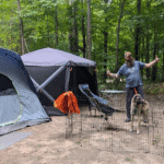 man standing in a pen with two dogs on a campsite next to two tents | Crown Land vs. Provincial Parks: Where's Better for Our Pets?