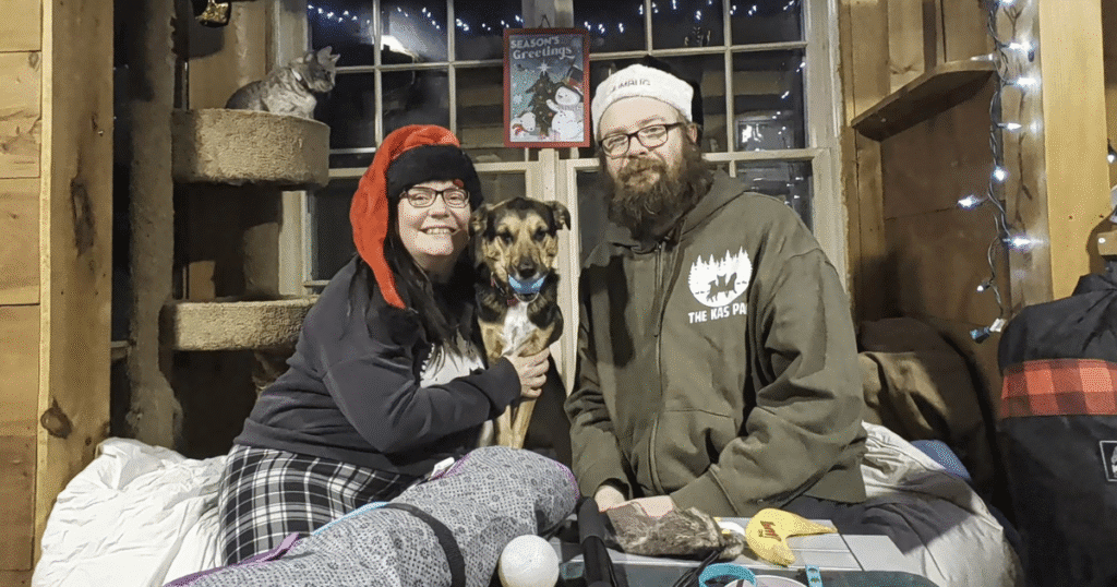couple sitting with their dog in front of a holiday themed backdrop | 2025 Holiday Gift Guide for Pets Who Love the Outdoors